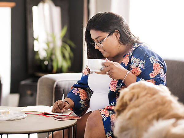Shot of an attractive woman writing in her diary while sitting in living room with a cup of coffee